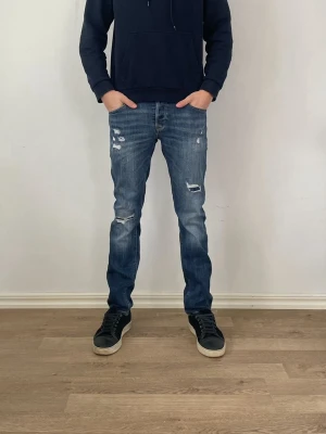 Jack and Jones Jeans - Säljer ett par riktigt fräscha blåa jack and jones jeans med slitningar endast för 449kr!                                                                             Nypris:999kr därav väldigt bra erbjudande.             Modell:slim fit                                                          Har några frågor är det bara att fråga på!