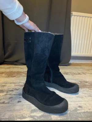 Canada goose stövlar - Säljer ett par svarta höga stövlar från Canada goose i mocka med grov gummisula. Stövlarna har dragkedja på sidan och en liten logga upptill. Insidan verkar vara fodrad för extra värme. Perfekta för kalla dagar.