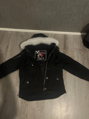Svart dunjacka Moose Knuckles - Säljer en svart dunjacka från Moose Knuckles med avtagbar huva och vit fuskpäls. Jackan har flera fickor med tryckknappar, dragkedja framtill och detaljer i metall. Perfekt för kalla vinterdagar och riktigt snygg streetstil.Exklusiv och varm vinterjacka från Moose Knuckles – perfekt för kalla dagar. Jackan kombinerar stilren design med högkvalitativa material och ger både maximal värme och komfort. Den är vind- och vattenavvisande, har en lyxig känsla och en passform som sitter snyggt