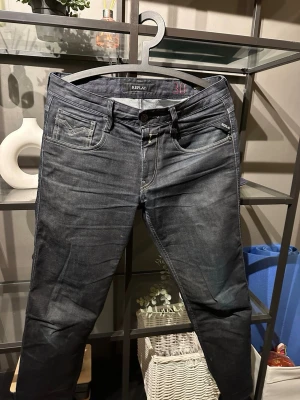 Mörkblå Replay jeans med slitningar - Säljer ett par mörkblå jeans från Replay med snygga slitningar och tvättade detaljer. Klassisk femficksmodell med smal passform och kontrastsömmar. Märkeslogga på fickan och bakfickan har en cool reva för extra edge. Perfekta för dig som gillar streetstyle.