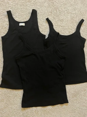 Svarta linnetoppar från Gina Tricot - Tre svarta linnetoppar från Gina Tricot i modellen 'basically basics'. Klassisk rak passform med breda axelband och rundad halsringning. Perfekta att styla lager på lager eller till jeans och kjol. Materialet är mjukt och stretchigt för extra komfort.