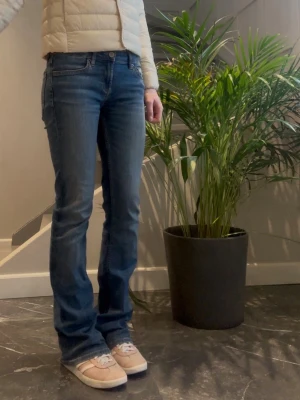 Blå bootcut jeans med låg midja - Säljer ett par klassiska blå bootcut jeans med låg midja och femficksmodell. Jeansen har en snygg tvätt och subtila slitningar för en avslappnad look. 