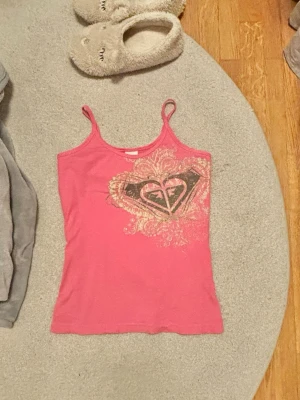 Rosa vintage linne från Roxy  - Säljer ett rosa linne från Roxy med tunna axelband och ett stort, dekorativt tryck framtill. Materialet är mjukt och stretchigt, perfekt för sommaren. Jättefint vintage linne!! 🦩