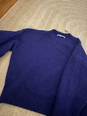 Mörkblå stickad tröja från Zara - En snygg mörkblå stickad tröja från Zara med klassisk rund halsringning och ribbstickade detaljer. Perfekt för att hålla sig varm under kyliga dagar. Materialet är mjukt och skönt, vilket gör den riktigt bekväm att bära.