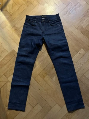 Mörkblå jeans från J.Lindeberg - Snygga mörkblå jeans från J.Lindeberg med klassisk femficksmodell och raka ben. Jeansen har en stilren look och är tillverkade i ett slitstarkt denimtyg. Perfekta för dig som gillar en enkel men trendig stil.