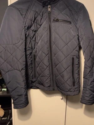 Mörkblå quiltad jacka från replay - Snygg mörkblå quiltad jacka med raka linjer och tre dragkedjefickor framtill. Jackan har hög krage med knapp och långärmad design. Perfekt för dig som gillar stilren och modern look.