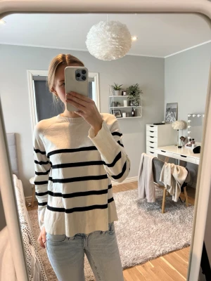 Vit stickad tröja med svarta ränder - Säljer en vit stickad tröja med svarta horisontella ränder. Tröjan har rund halsringning, långa ärmar och ribbstickade muddar. Passar perfekt till jeans och har en avslappnad, trendig look.