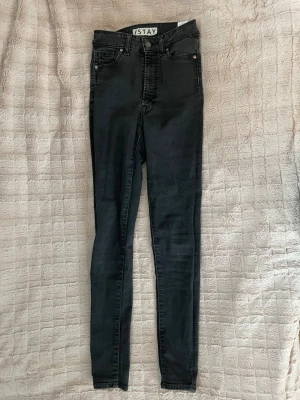 Svarta skinny jeans från Stay - Säljer ett par svarta skinny jeans från Stay med hög midja och klassisk femficksdesign. Jeansen har en tight passform och stretchigt material som sitter snyggt längs benen. Perfekta till en avslappnad eller trendig look.