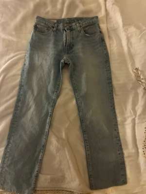 Ljusblå raka jeans från Levi's - Säljer ett par klassiska ljusblå jeans från Levi's med rak passform och fem fickor. Jeansen har hög midja och är tillverkade i slitstark denim. Perfekta för en avslappnad och tidlös stil. Längd 65 från gren till slutet och ben (inner), midja 37 cm från ena sidan till andra. Storlek 32/25