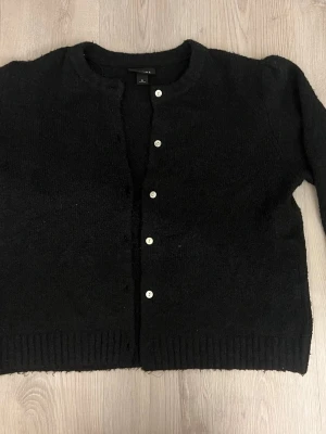 Svart stickad kofta  - Mysig svart stickad kofta från Monki med rund halsringning och vita knappar framtill. 