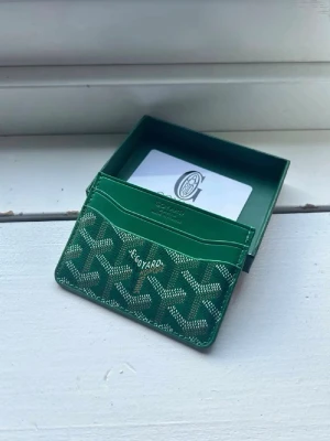 Grön kortfodral från Goy4rd - Snyggt grönt kortfodral från Goy4rd med det klassiska mönstret i vitt och beige. Fodralet har flera fack för kort och är gjort i exklusivt läder med tryckt logotyp framtill. Perfekt för dig som vill ha en stilren och lyxig accessoar i fickan.