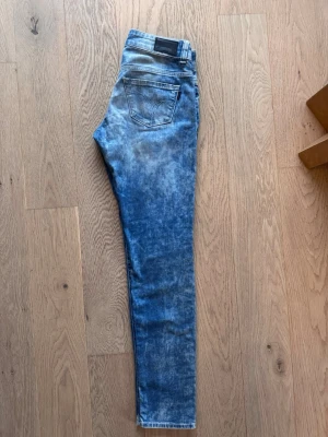 Blå tvättade skinny jeans 320 - Snygga blå skinny jeans med tvättad effekt och klassisk femficksdesign. Jeansen har normalhög midja, smala ben och detaljerade sömmar på bakfickorna. Perfekta för en avslappnad och trendig look. Modell 320. W28/L32.