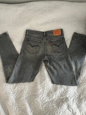 Grå Levi's jeans - Säljer ett par grå jeans från Levi’s. Jeansen har en snygg tvättad look, kontrastsömmar och den ikoniska läderpatchen bak i midjan. Perfekta för en avslappnad och trendig stil.
