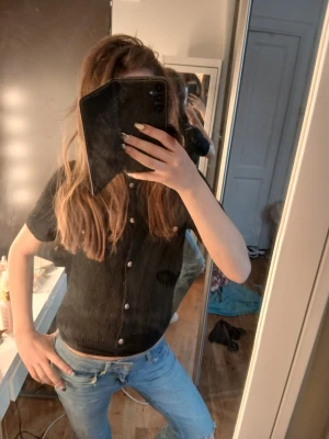 Svart kortärmad stickad topp från gina - Snygg svart topp med korta ärmar och knappar framtill. Modellen är figurnära och toppen har en enkel, stilren look som passar till mycket. Perfekt att matcha med jeans eller kjol för en trendig outfit. Stl 158/164 från gina tricot