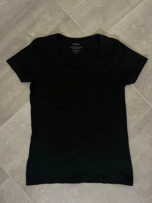 Svart basic t-shirt från Newbody - En enkel och stilren svart t-shirt från Newbody med rund halsringning och korta ärmar. Tillverkad i mjuk bomull som känns skön mot huden. Perfekt till alla typer av outfits och lätt att matcha med andra plagg.