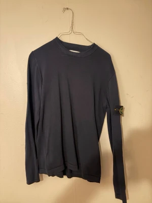 Mörkblå långärmad Stone Island tröja - Snygg mörkblå långärmad tröja från Stone Island med klassisk rund hals och ikonisk logopatch på vänster ärm. Enkel och stilren design som passar perfekt till jeans eller cargobyxor. Materialet känns mjukt och bekvämt mot huden.