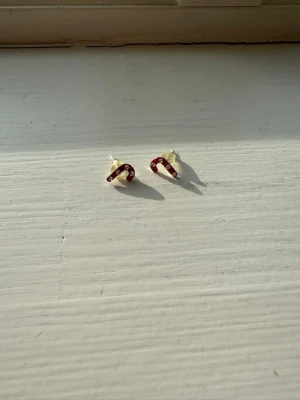 Örhängen med polkagrisar - Små örhängen i form av polkagrisar med röd och vit randig design. Sött och lekfullt motiv som passar perfekt för dig som gillar unika detaljer. Stiftmodellen gör dem enkla att bära och de är tillverkade i silver.