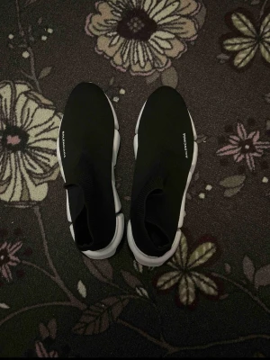 Balenciaga Speed Trainer svarta sneakers - Svarta Balenciaga Speed Trainer sneakers med vit chunky sula och stickad ovandel i textil. Minimalistisk design med Balenciaga-logga på sidan. Skorna har en strumpliknande passform och elastisk kant för enkel påtagning. Perfekta för dig som gillar streetwear och trendig stil.