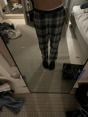 Rutiga pyjamasbyxor i svart och vitt - Säljer ett par pyjamasbyxor med svartvitt rutmönster och elastisk midja. Byxorna har raka ben och är tillverkade i ett mjukt, bekvämt tyg som passar perfekt för att chilla hemma. Klassisk och avslappnad stil som funkar året runt.
