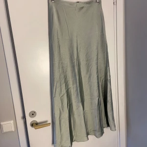 Ljusgrön långkjol i satin - Snygg ljusgrön långkjol i ett glansigt satinliknande material. Kjolen har en enkel, rak passform och faller mjukt längs benen. Perfekt för dig som gillar stilrena och minimalistiska plagg.