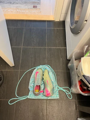 Nike Mercurial fotbollsskor turkos/rosa - Säljer ett par Nike Mercurial fotbollsskor i turkos med rosa detaljer och dobbar. Skorna har en strömlinjeformad design och är tillverkade i syntetmaterial för bästa grepp och känsla på planen. Medföljer matchande turkos skopåse.