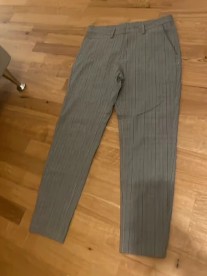Grå kostymbyxor med smal passform Zara - Snygga grå kostymbyxor från Zara med diskret rutmönster och smal passform. Byxorna har fickor i sidorna och hällor för bälte. Perfekta för en stilren look och passar till skjorta eller t-shirt.