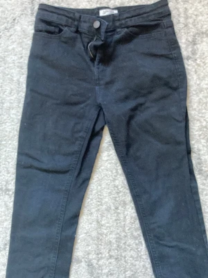 Svarta trekvarts skinny jeans från Lindex - Säljer ett par svarta trekvarts skinny jeans från Lindex i storlek 152. Klassisk femficksmodell med knapp och dragkedja framtill. Jeansen har smal passform och är tillverkade i ett stretchigt material för extra komfort.