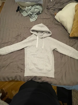Ljusgrå hoodie från Russemerch - Ljusgrå hoodie från Russemerch med klassisk huva och vita dragsnören. Hoodien har en stor magficka framtill och ribbade muddar vid ärmslut och nederkant. Tillverkad i mjukt sweatshirtmaterial, perfekt för en avslappnad stil.