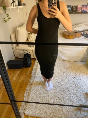Svart ribbad långklänning - Säljer en svart ribbad långklänning med smala axelband och figurnära passform. Klänningen är ärmlös och har en enkel, stilren design som passar perfekt till många olika tillfällen. Materialet känns mjukt och stretchigt.