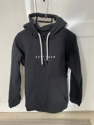 Svart hoodie från Dope Snow XXS - Säljer en svart hoodie från Dope Snow med vit text och grafiskt tryck på ryggen i rosa, blått och vitt. Hoodien har stor huva, vita dragsnören och en magficka. Perfekt för dig som gillar streetwear och snygga detaljer.