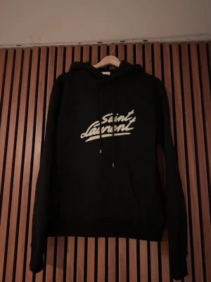 Saint Laurent hoodie - Tja säljer denna feta saint Laurent hoodien. Hoodien är i toppskick och tagen medföljer. Den är i väldigt tjockt material därmed perfekt för vintern/våren. På bild 6 kan man se att det inte är något Kina tryck och är riktigt hög kvalité. Storlek S står 170. Passar mig som är 177 (bild 7) Hör av er vid frågor eller bilder!🌟🫡
