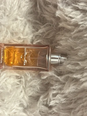 Senteur de caia Eau de Parfum - Snygg parfymflaska från Senteur de Caia i glas med rektangulär form och silverfärgad spraykork. Flaskan har en varm orange ton på vätskan och minimalistisk text på framsidan. Perfekt för dig som gillar stilrena och moderna dofter. Har tappat bort locket också så att ni vet