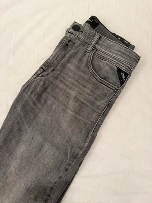Grå slim fit jeans från Replay - Snygga grå slim fit jeans från Replay med klassisk femficksdesign och diskret tvättad look. Jeansen har normal midja, dragkedjegylf och är tillverkade i en mjuk bomullsblandning med lite stretch för extra komfort.