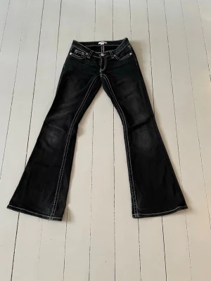 Svarta lågmidjade bootcut jeans från Gina Tricot  - Säljer ett par svarta bootcut jeans med vita kontrastsömmar och broderade bakfickor. Jeansen har låg midja och Bootcut model. Storlek xs. Säljer då jag tyvärr har växt ur dem. Är lite slitna i nederkanten ( bild fyra ) men har annars inga skador. 
