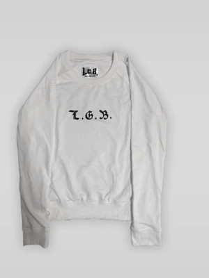 Vit sweatshirt från L.G.B. med tryck - Säljer en vit sweatshirt från L.G.B. med svart text 'L.G.B.' på bröstet och stort tryck med dödskalle och texten 'DEAD OR ALIVE' på ryggen. Tröjan har rund hals och ribbade muddar. Perfekt för dig som gillar streetwear och edgy detaljer.