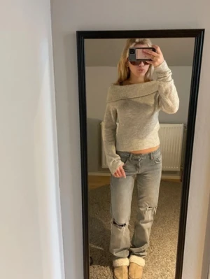 Ljusgrå off shoulder stickad tröja - Säljer en ljusgrå stickad tröja med off shoulder-design och bred krage. Tröjan är croppad och har långa ärmar med avslappnad passform. Materialet är mjukt och stretchigt stickat tyg.
