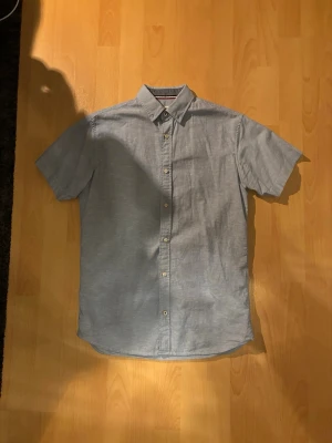 Ljusblå linneskjorta Jack & Jones - Säljer en ljusblå linneskjorta från Jack & Jones med korta ärmar och klassisk krage. Står storlek XS men passar som S. Skjortan har knappar framtill och är gjord i mjuk bomull, perfekt för en clean och enkel stil. Passar dig som gillar minimalistiskt och stilrent.