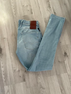 Ljusblå  jeans från Replay - Säljer ett par ljusblå  jeans från Replay med klassisk femficksdesign och läderpatch bak i midjan. Jeansen har en snygg tvättad look och är tillverkade i mjukt denimtyg som sitter tight hela vägen ner.