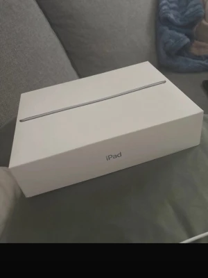 Apple iPad  med originalkartong - Säljer en svart Apple iPad  och originalkartong. Surfplattan har en stor skärm, rundade hörn och klassisk Apple-design. Perfekt för streaming, surf och appar. Laddas via lightning-kabel och har en stilren vit förpackning.