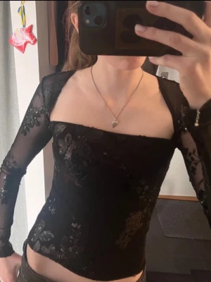 Festtopp - Snygg svart mesh topp med blommigt mönster och transparenta långärmar. Toppen har en fyrkantig urringning och sitter tight. Perfekt för dig som vill ha en trendig och elegant look. Använd 1 gång! Säljer då jag tyvärr inte använder den💕passar xs-s