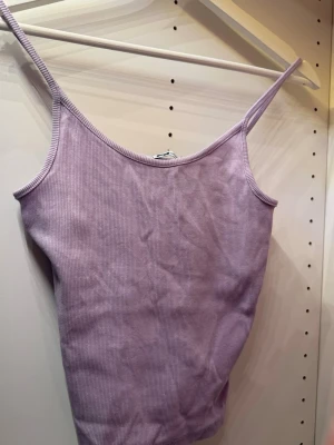 Ljuslila ribbad linnetopp - Säljer en ljuslila ribbad linnetopp med smala axelband. Toppen har en enkel och stilren design som passar perfekt till sommaren. Materialet är mjukt och stretchigt för en bekväm passform.