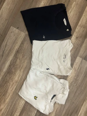3-pack t-shirts Ralph Lauren , Lyle & Scott, Gant - Säljer tre snygga t-shirts: en marinblå från Gant med liten logga, en vit från Polo Ralph Lauren med broderad häst och en vit från Lyle & Scott med gul logga. Alla har klassisk passform och rund hals. Perfekta basplagg till garderoben! Alla är äkta från kidsbrandstore. 