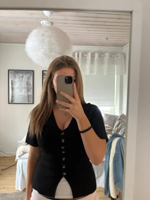 Svart v-ringad topp med knappar - Stilren svart topp från gina tricot i storlek S. Modellen har korta ärmar och en figurnära passform. Den är använd fåtal gånger, säljer då den inte kom till användning💗
