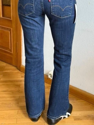 Blå bootcut jeans från Levi's - Säljer ett par klassiska blå bootcut jeans från Levi's med snygga bakfickor och kontrastsömmar. Jeansen har en låh  midja och är tillverkade i ett slitstarkt denimtyg. Perfekta för en avslappnad och trendig look.