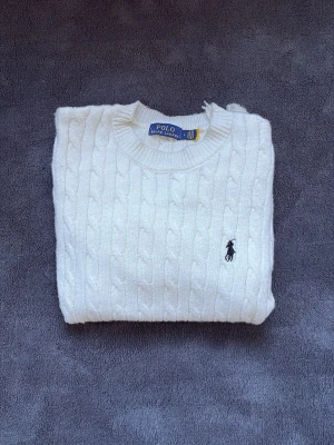 Polo Ralph lauren kabelstickad - Tidlös kabelstickad tröja från Polo Ralph Lauren i klassiskt vitt utförande. Ikonisk passform med broderad logga på bröstet.  En riktig garderobsklassiker – lika snygg till jeans som över skjorta.  Storlek: L passar mer som S/M Skick: Mycket bra