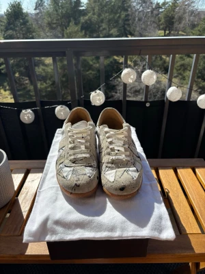 Skolyx sneakers med färgstänk - Unika sneakers från skolyx i vitt läder med svarta färgstänk och beige detaljer. Klassisk låg modell med vita snören och gummisula. Perfekta för dig som vill sticka ut med en kreativ och trendig look.