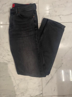 Grå/Svarta Hugo jeans W31 - Snygga grå/svarta jeans från Hugo med diskret tvättad look och klassisk femficksmodell. Jeansen har en tydlig röd Hugo-logga på bakfickan som ger en cool kontrast. Tillverkade i mjukt denimtyg som sitter skönt och passar till många olika stilar. De är andvända max 3 gånger. Nypris är cirka 1200:- men jag kan släppa de för 649:-, priset är inte ristat i sten så det går att diskutera genom en smidig affär. Tveka inte att höra av dig om du har några vidare funderingar🙌