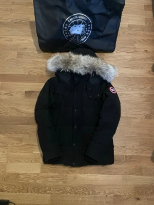 Canada Goose jacka - Säljer en svart dunjacka från Canada Goose med avtagbar huva och äkta pälsdetalj. Jackan har klassisk patch på ärmen, flera fickor och stängs med dragkedja och knappar. Perfekt för kalla vinterdagar och riktigt varm.