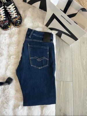 Mörkblå jeans från replay - Snygga mörkblå stretchiga jeans från replay med klassisk femficksmodell och kontrastsömmar. Bakfickan har en unik broderad detalj och byxorna har en svart patch vid linningen. Perfekta för dig som gillar stilrena och tidlösa jeans. Storlek 32/32. Skicka till mig för fler bilder eller info!