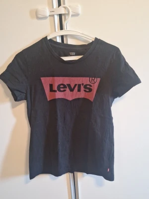 Svart Levi's t-shirt med logga strl S - Klassisk svart t-shirt från Levi's med den ikoniska röda loggan tryckt på bröstet. Katt finns i hemmet. Men rollar av hår och fraktar snabbt